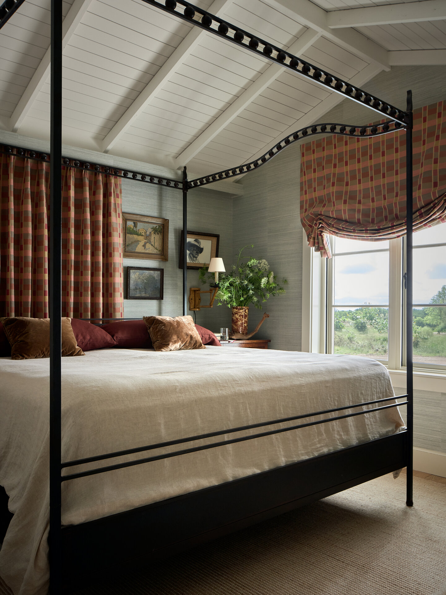 Luxurious bedroom with a black canopy bed, plaid curtains, and a view of greenery outside.